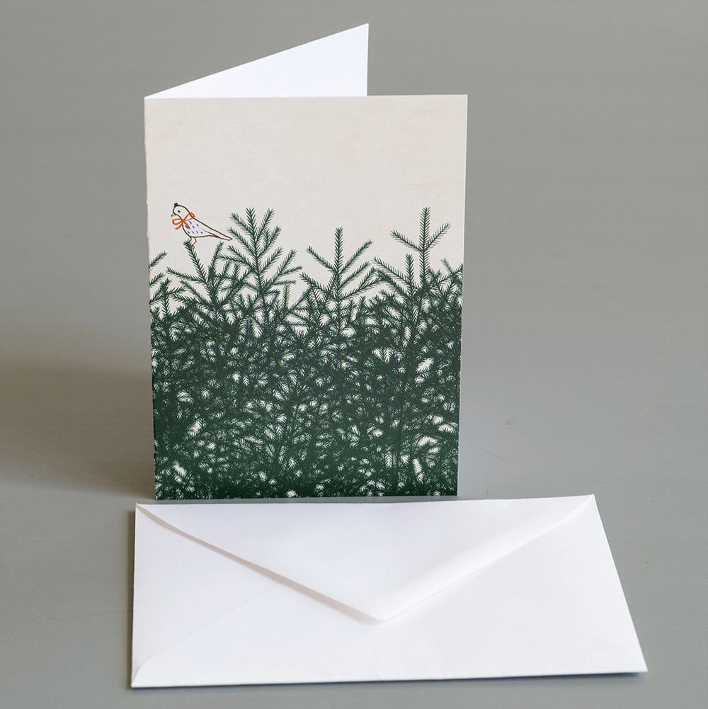 The Bow Birdie Card w. Envelope A6 by Fine Little Day features a bird perched on pine branches and is shown standing behind a plain white envelope on a gray surface.