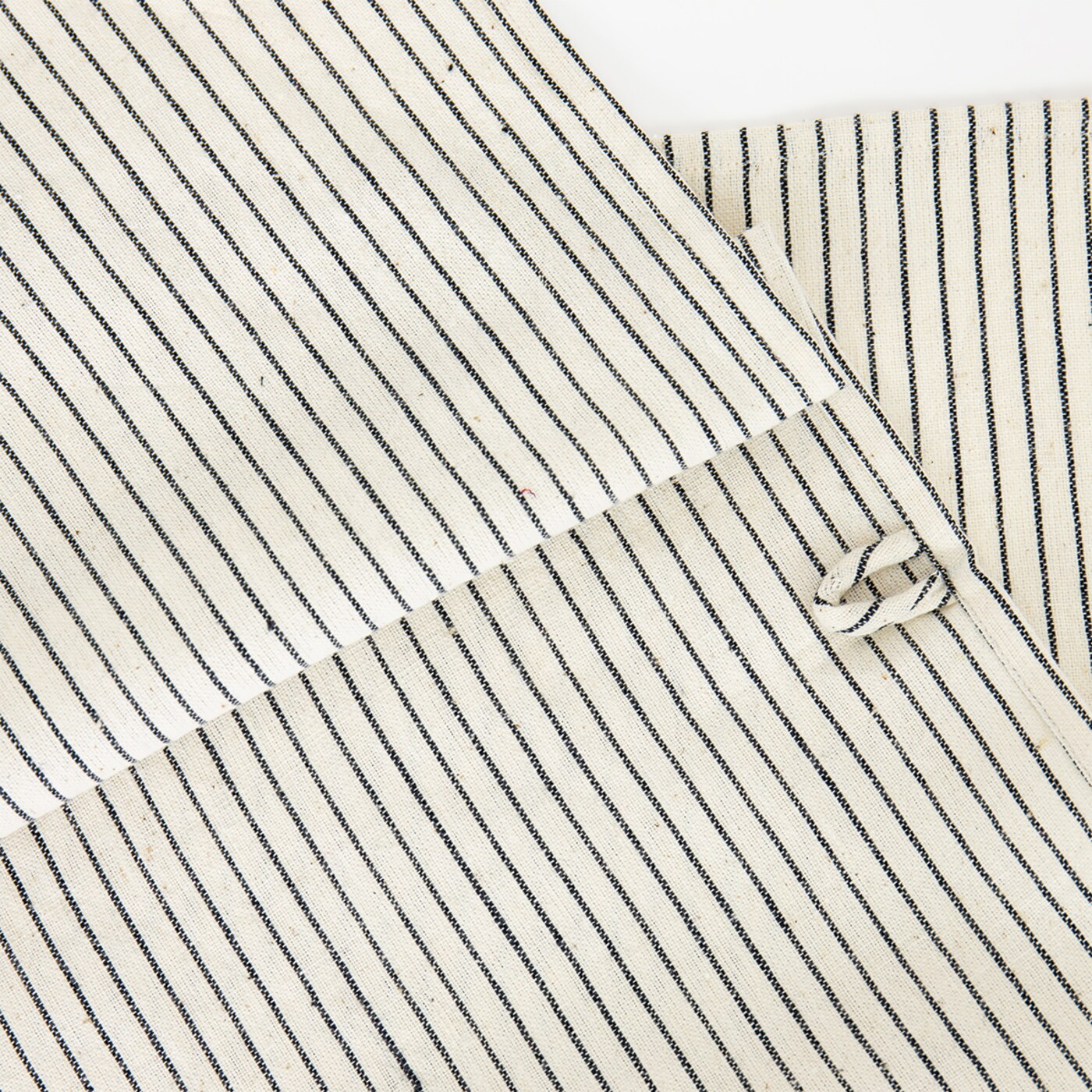 A close-up of A World of Craft’s hand-woven eco cotton Towel, Thinstripe in Black & White, shows overlapping pieces with thin black stripes on beige and a fabric loop detail on the right.