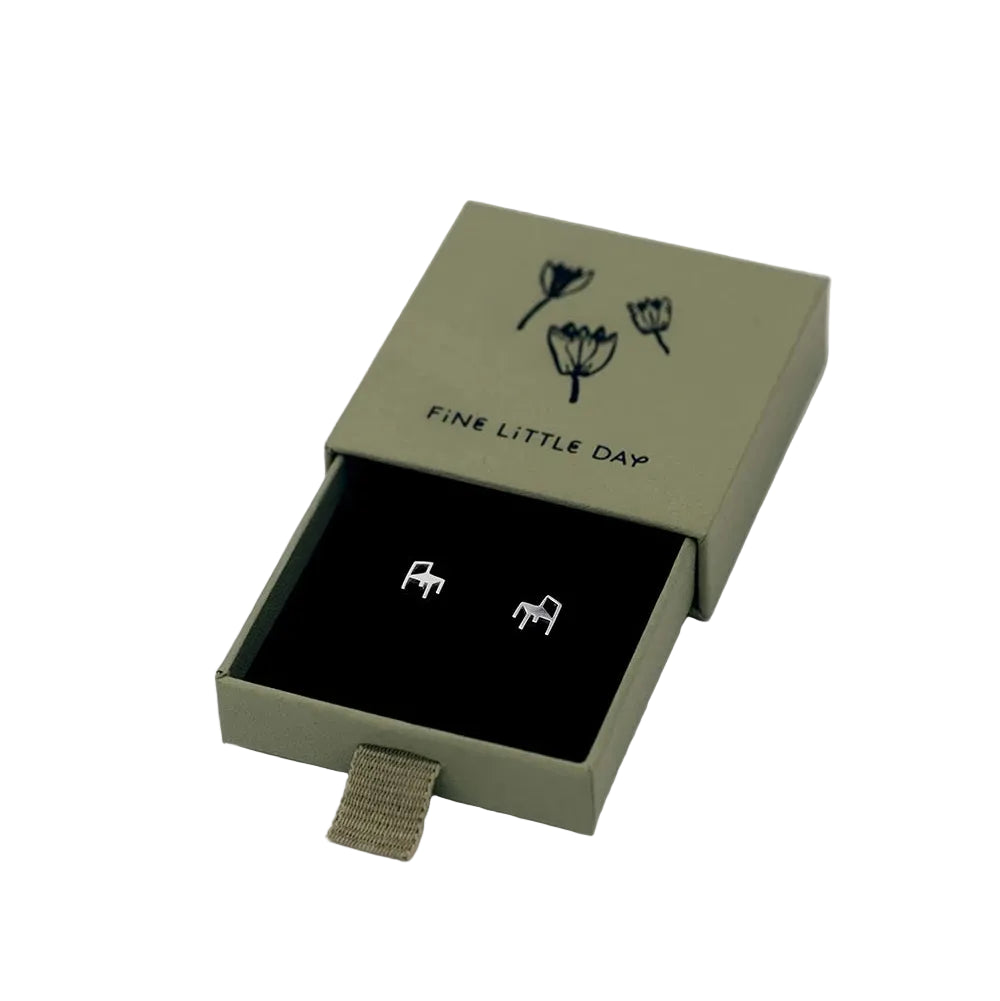 A pair of Chair Stud Earrings in Silver by Fine Little Day, crafted from sterling silver and shaped like small chairs. Presented in an open green box adorned with black floral illustrations and the brand name “FINE LITTLE DAY” on the lid, these unique stud earrings are inspired by orchestra chairs and offer a playful take on elegant seating.