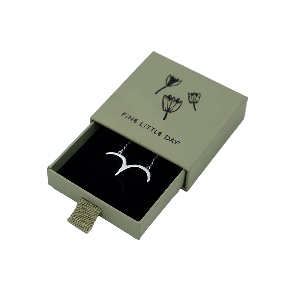 A green jewelry box with black floral illustrations from Fine Little Day holds the Bird Necklace in Silver—a 925 sterling silver necklace featuring a delicate bird pendant. The box is partially open, revealing the necklace displayed on a black insert inside.