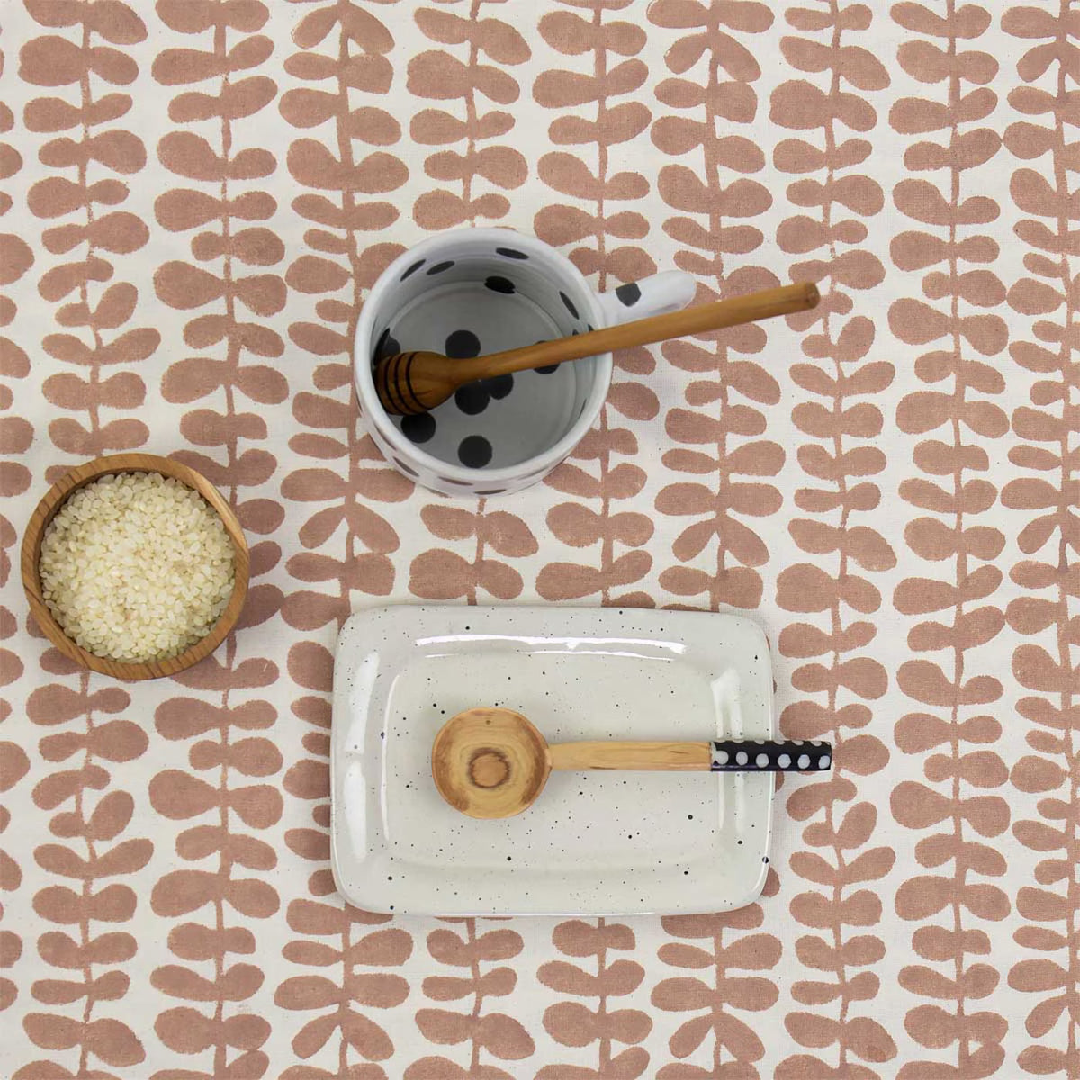 The Tablecloth Foliage in Pink & Off White by A World of Craft (140 cm x 260 cm, handmade) displays a bowl of rice, a dotted white cup with honey dipper, and a rectangular plate with a wooden spoon.