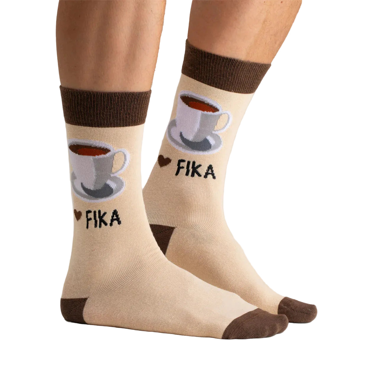 A pair of Svensk Husman Socks, Coffee Cup Fika: beige socks with brown toes, heels, and cuffs. Each features coffee cup patterns, "FIKA," and a heart—celebrating Swedish culture. Worn on feet.