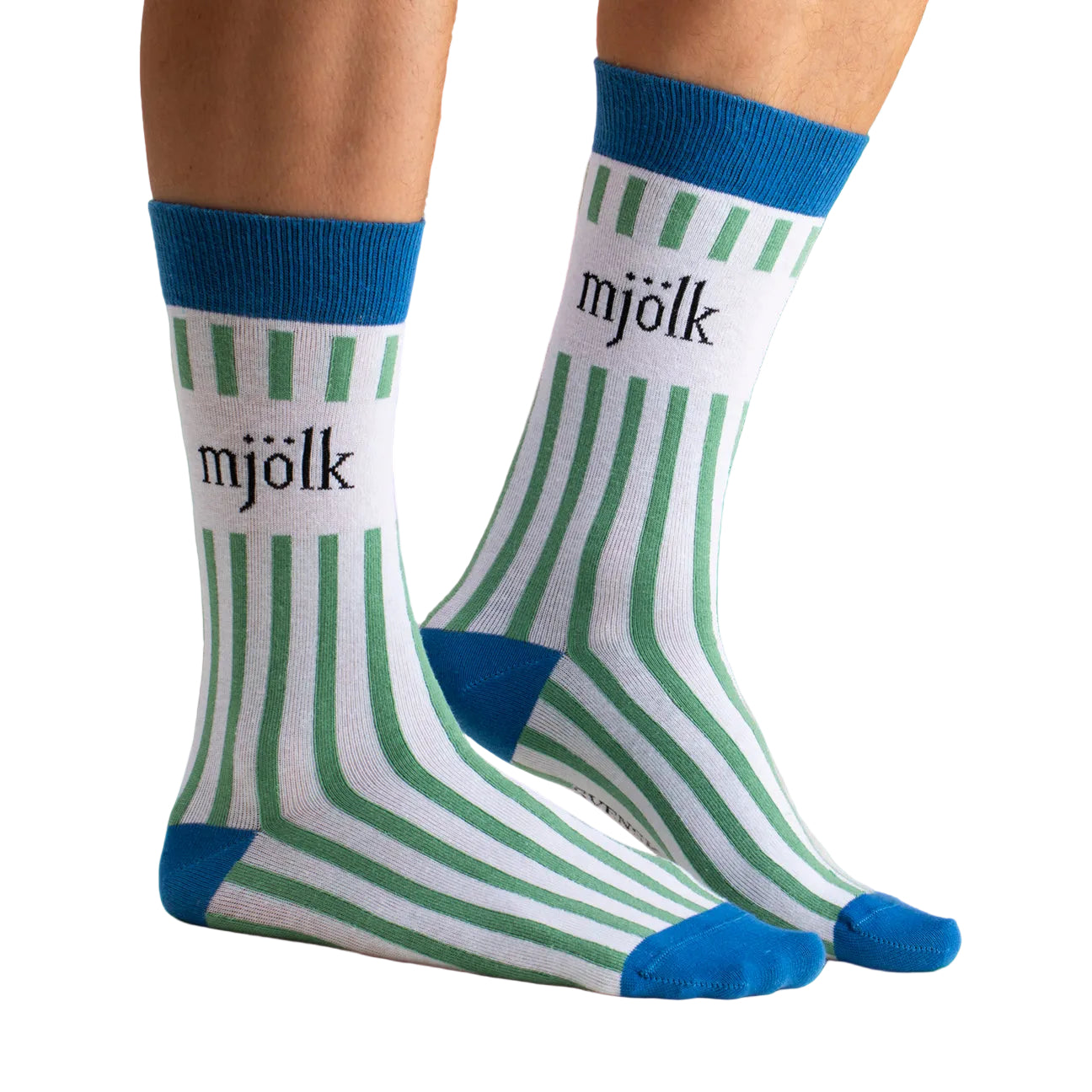 Two feet wear Svensk Husman’s Grön Mjölk socks—a playful cotton blend with white fabric, green stripes, blue toes, heels, and cuffs. "mjölk" is printed in black on the sides of these Swedish socks.