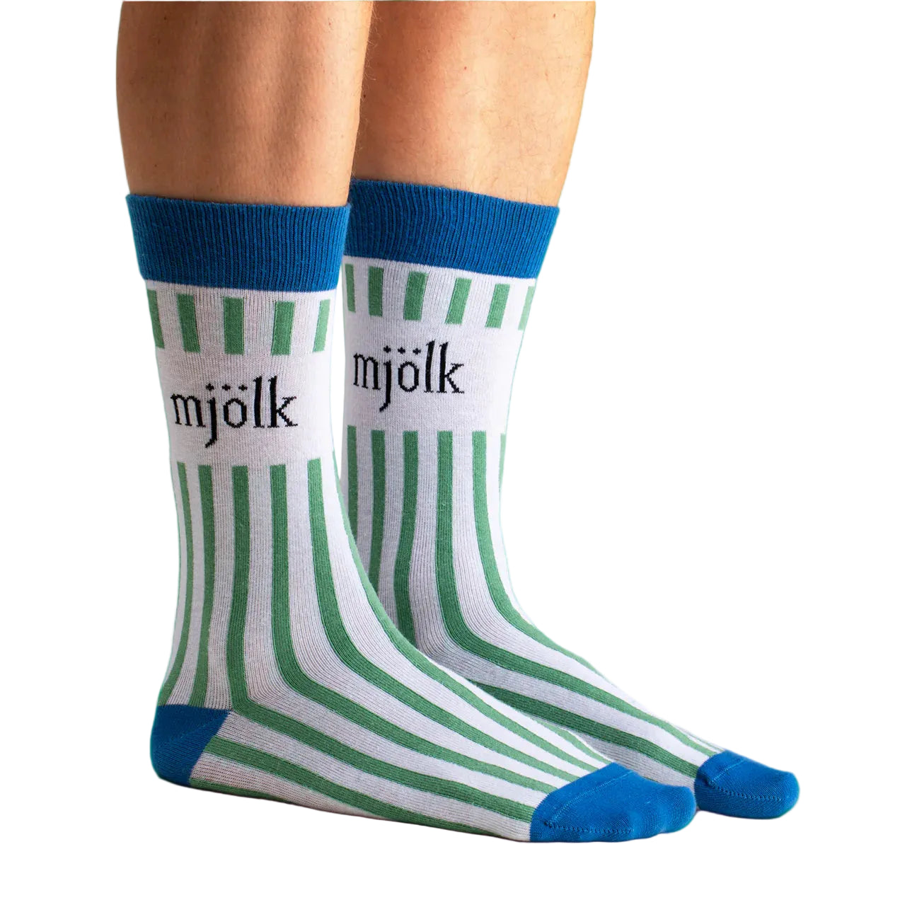 A pair of feet in Svensk Husman Socks' Grön Mjölk (Green Milk) socks—white with green stripes, blue toes, heels, and cuffs. "Mjölk" in black on the side. Made from a soft cotton blend for comfortable Swedish style.