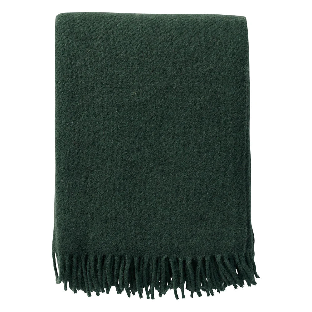 A folded Klippan Yllefabrik Gotland Throw in Gotland wool and lambswool, in bottle green with fringed edges, displayed against a white background.