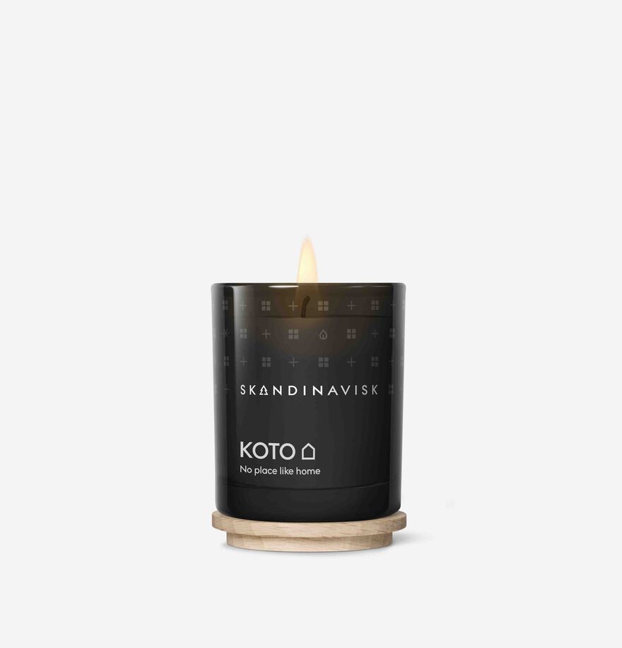 A lit Skandinavisk Mini Scented Candle Koto 20h, 65g, made from Swedish rapeseed wax, sits on a round wooden base against a plain white background.