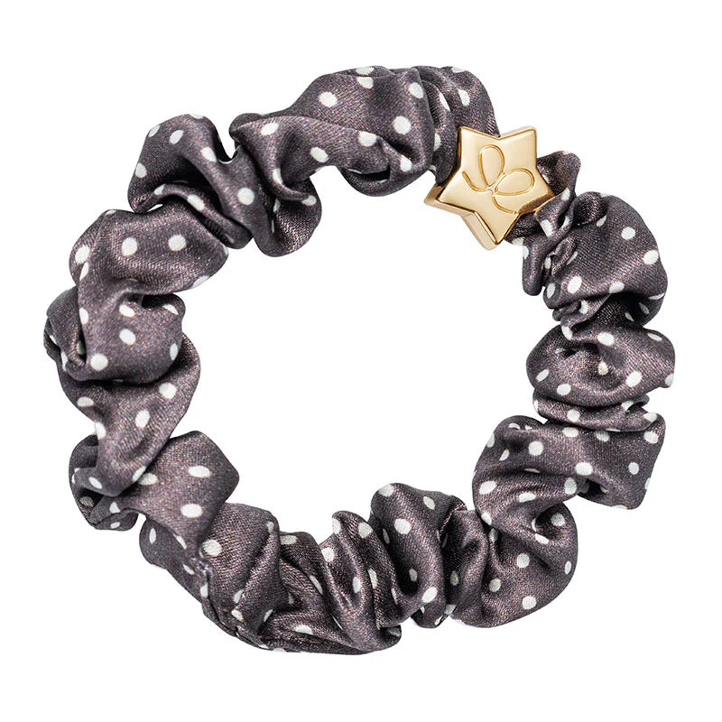The ByEloise Silk Scrunchie in Polka Dot Mocha features white dots and a gold star-shaped charm, offering a snag-free hair accessory that brings playful elegance to any hairstyle.