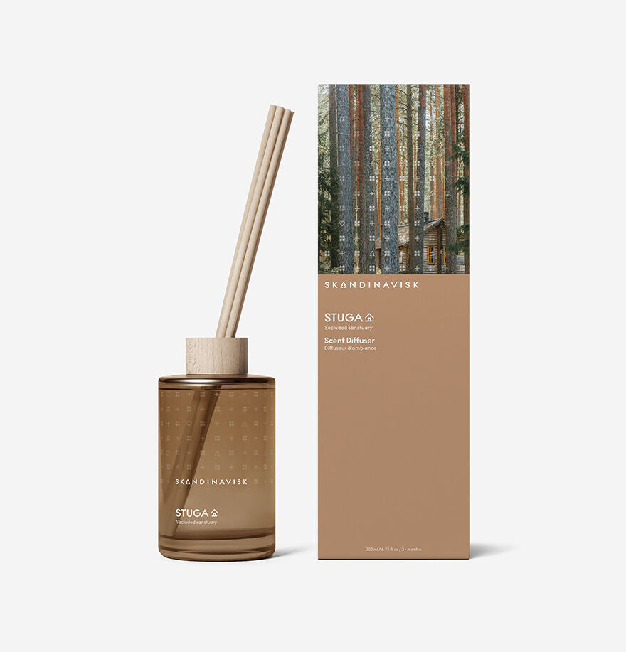 The Skandinavisk Scent Diffuser Seasonal Stuga (200ml) features a brown bottle with wooden sticks and offers a vegan fragrance to enhance your room.