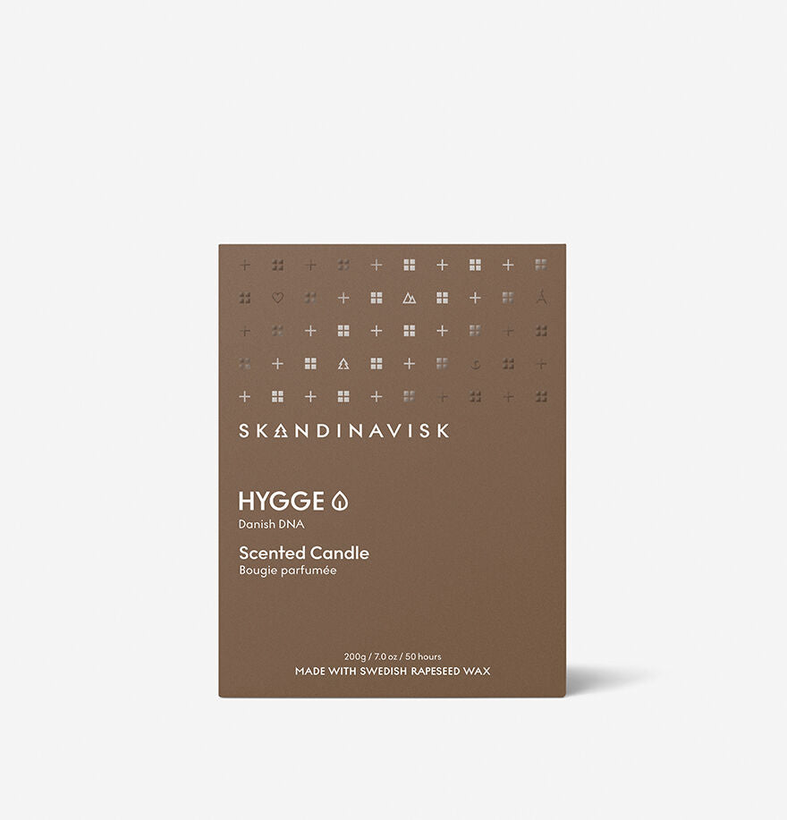 A brown rectangular box of Skandinavisk Scented Candle Hygge 50h, 200g, with white text and minimalist symbols, made from Swedish rapeseed wax, is shown against a plain light background.