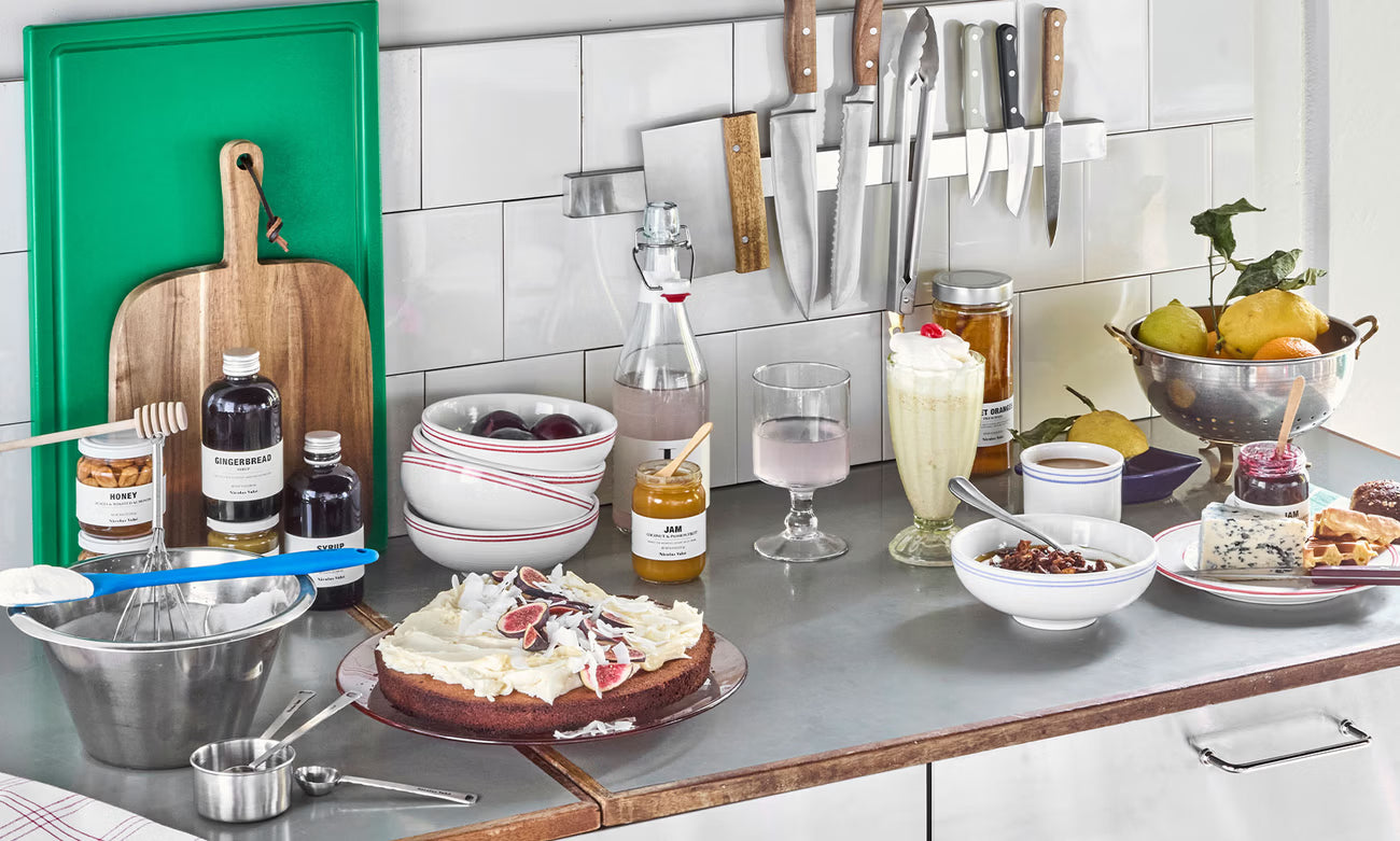 Kitchen counter with cake, drinks, and utensils on a tiled wall background