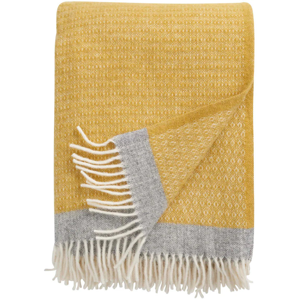 The Harald Eco Lambswool Throw in Yellow by Klippan features a subtle pattern, gray border, and white fringed edges. A corner is flipped to display both colors and fringe, adding cozy, stylish appeal to any home.