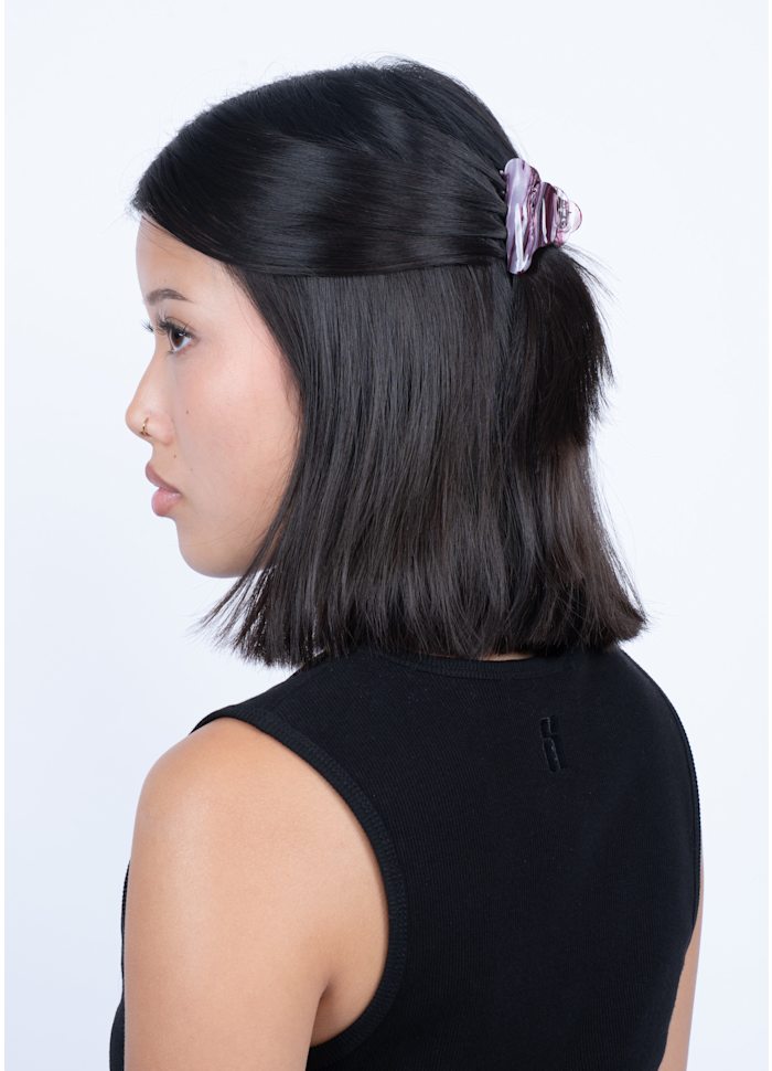 A person wearing a pink and purple marbled Sui Ava Lene Ember Mini Hair Claw Clip holding back a section of their dark hair.