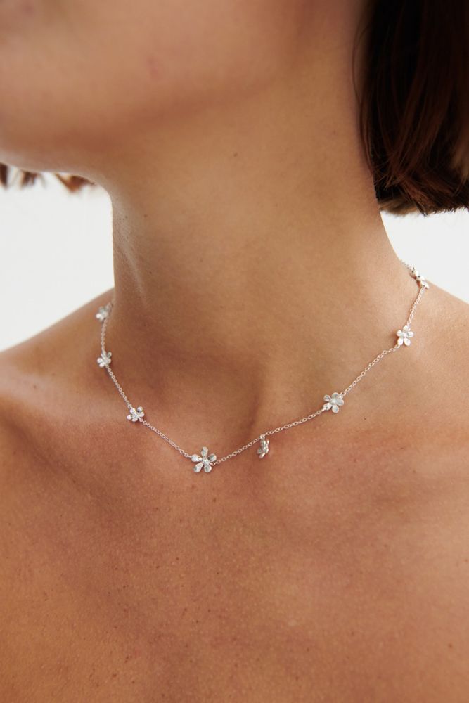 A close-up of a woman’s neck wearing the Wild Poppy Necklace in Gold by Pernille Corydon, this Nordic-inspired summer jewelry features delicate flower charms and evokes elegance against a plain light background.