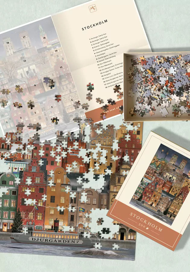 A partially completed Martin Schwartz Christmas in Stockholm Puzzle (500 pieces) lies on a table, displaying festive Stockholm buildings. Nearby are the matching puzzle box, loose pieces, and a landmark list for added holiday cheer.