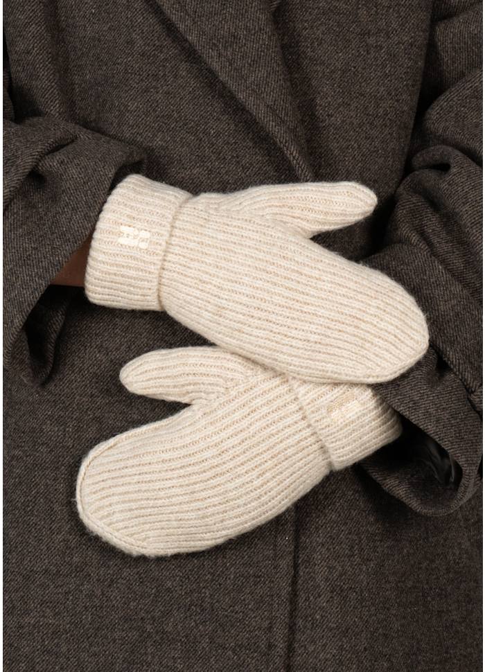 A person wearing a dark coat has their arms crossed, showing off a pair of Sui Ava’s Brenda Mittens in Beige—chunky knit mittens that add a cozy touch to the ensemble.