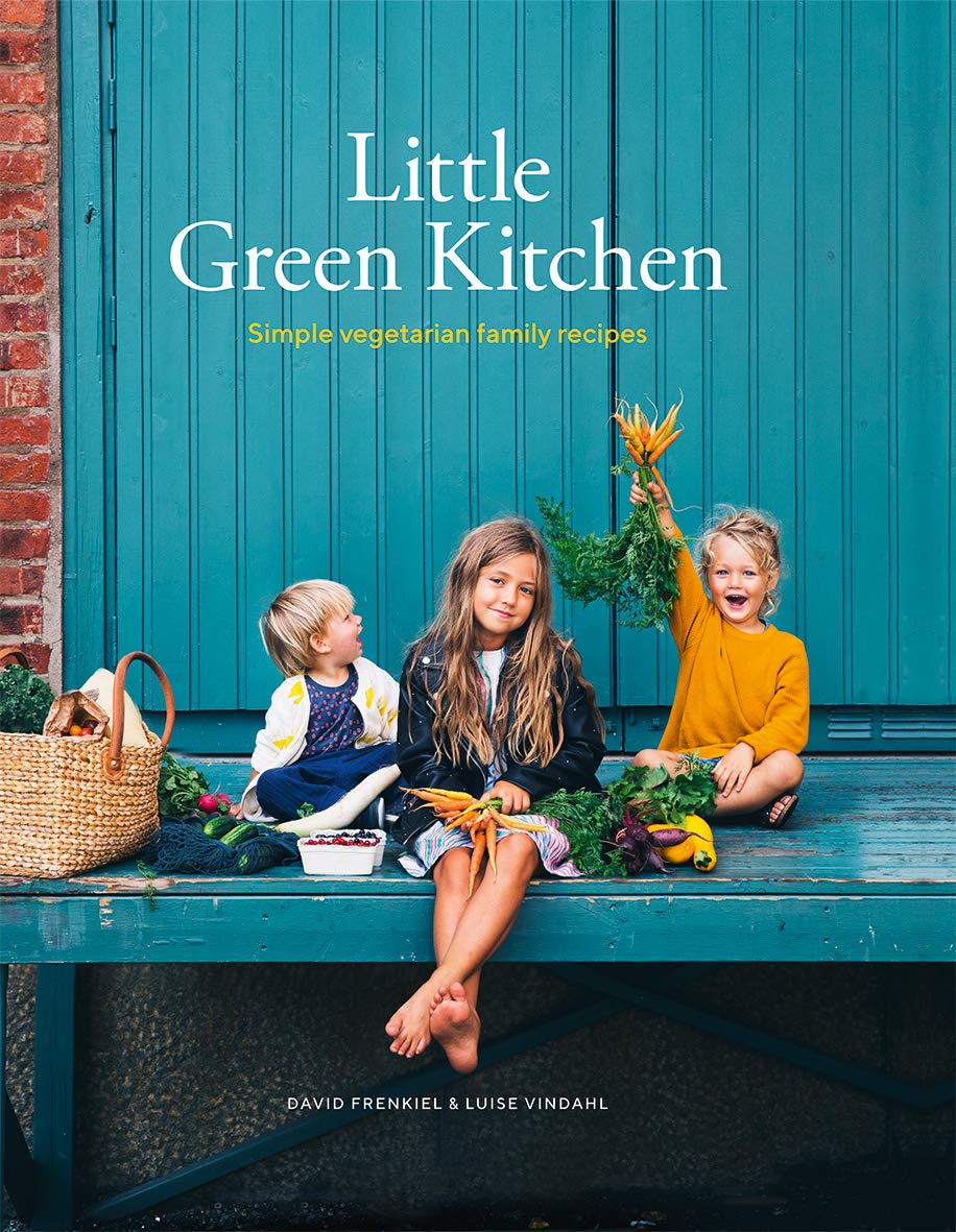 Three children sit barefoot on a blue bench with fresh vegetables, in front of a blue wall. The book cover features Little Green Kitchen - Simple Vegetarian Family Recipes by Little Green Kitchen, with wholesome family-friendly meals.