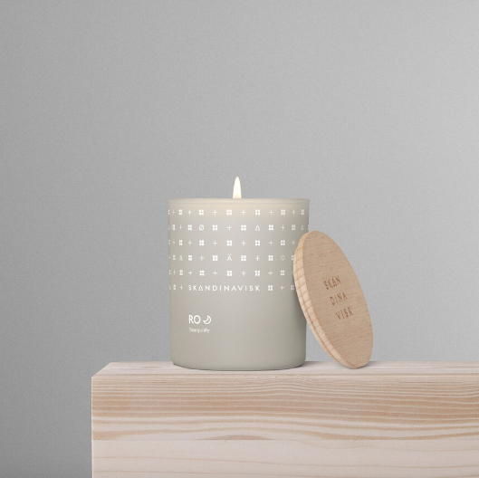 The Skandinavisk Scented Candle Ro 50h, 200g, crafted with Swedish rapeseed wax, rests on a light wooden surface with its wooden lid beside it, exuding calm elegance.