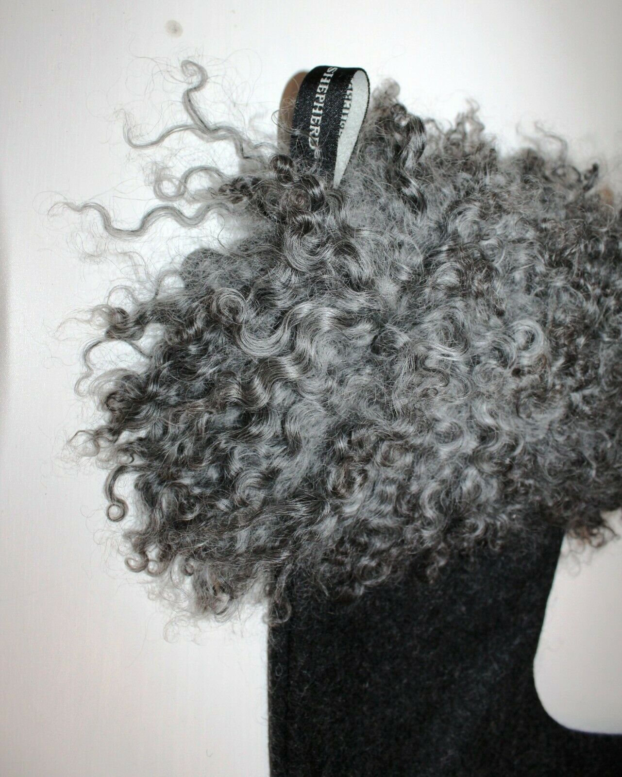 A close-up of Shepherd of Sweden’s Christmas Stocking, Franni in black sheepskin, featuring a thick curly fur trim and branded pull tab, set against a white background.