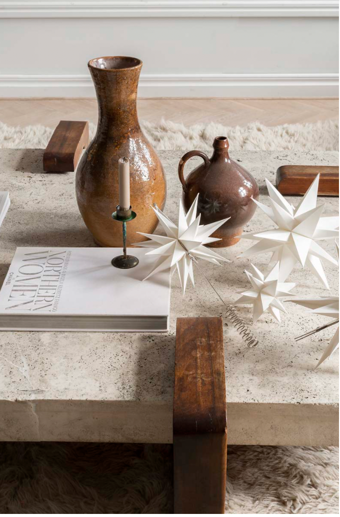 A stone coffee table with two ceramic vases, a candlestick, a book, wooden accents, and the Watt & Veke Topstar Sputnik handmade paper Christmas tree topper (25cm) sits atop a light shag rug.