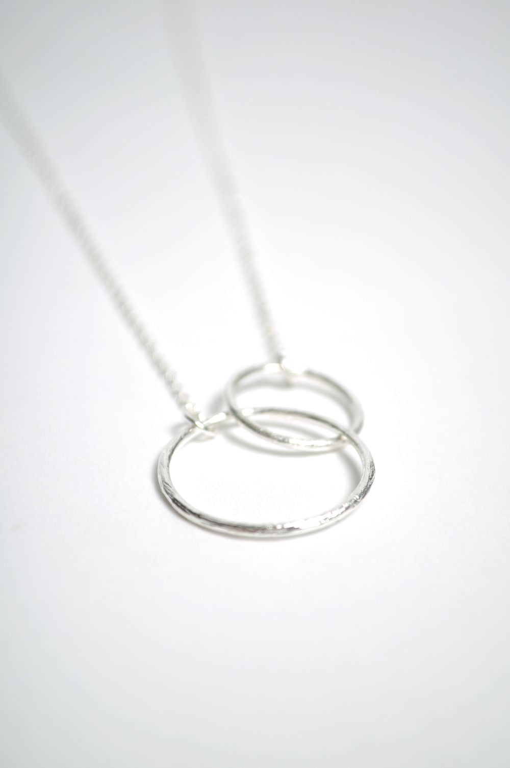 The Double Plain Ring Necklace in Silver by Pernille Corydon features interlocking circle pendants on a fine chain, displayed on a white background for a minimalist look.