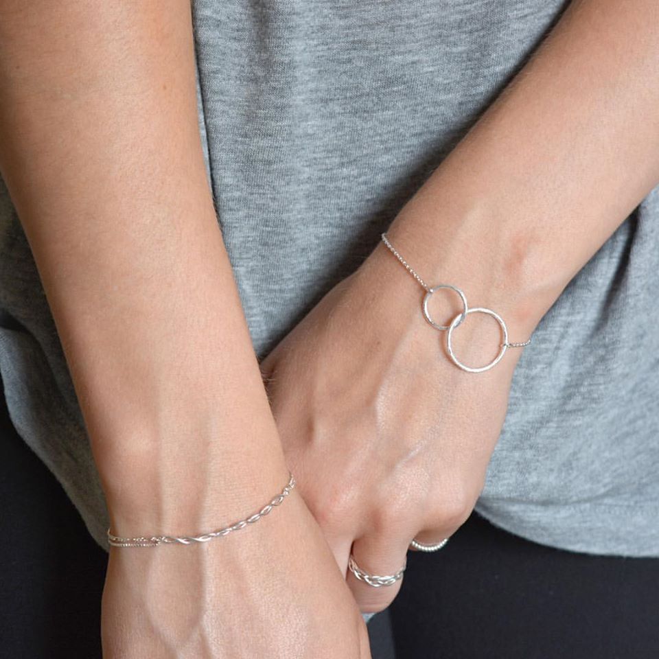 Close-up of hands wearing Pernille Corydons Double Plain Ring Bracelet in Silver—featuring two interlocking circles for a modern, elegant look. Styled with a gray shirt.
