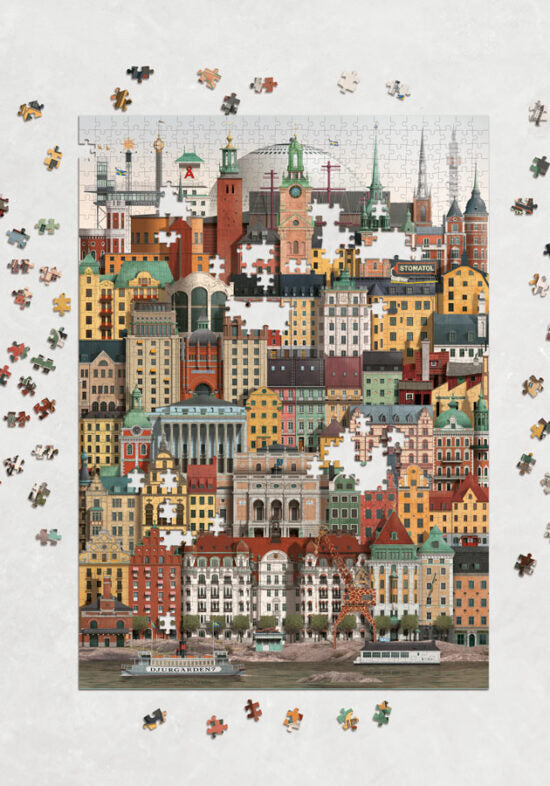 The Martin Schwartz Stockholm City Puzzle (1000 Pieces) features a vibrant cityscape with detailed buildings, shown mostly assembled with some pieces missing and loose puzzle pieces scattered on a white surface.