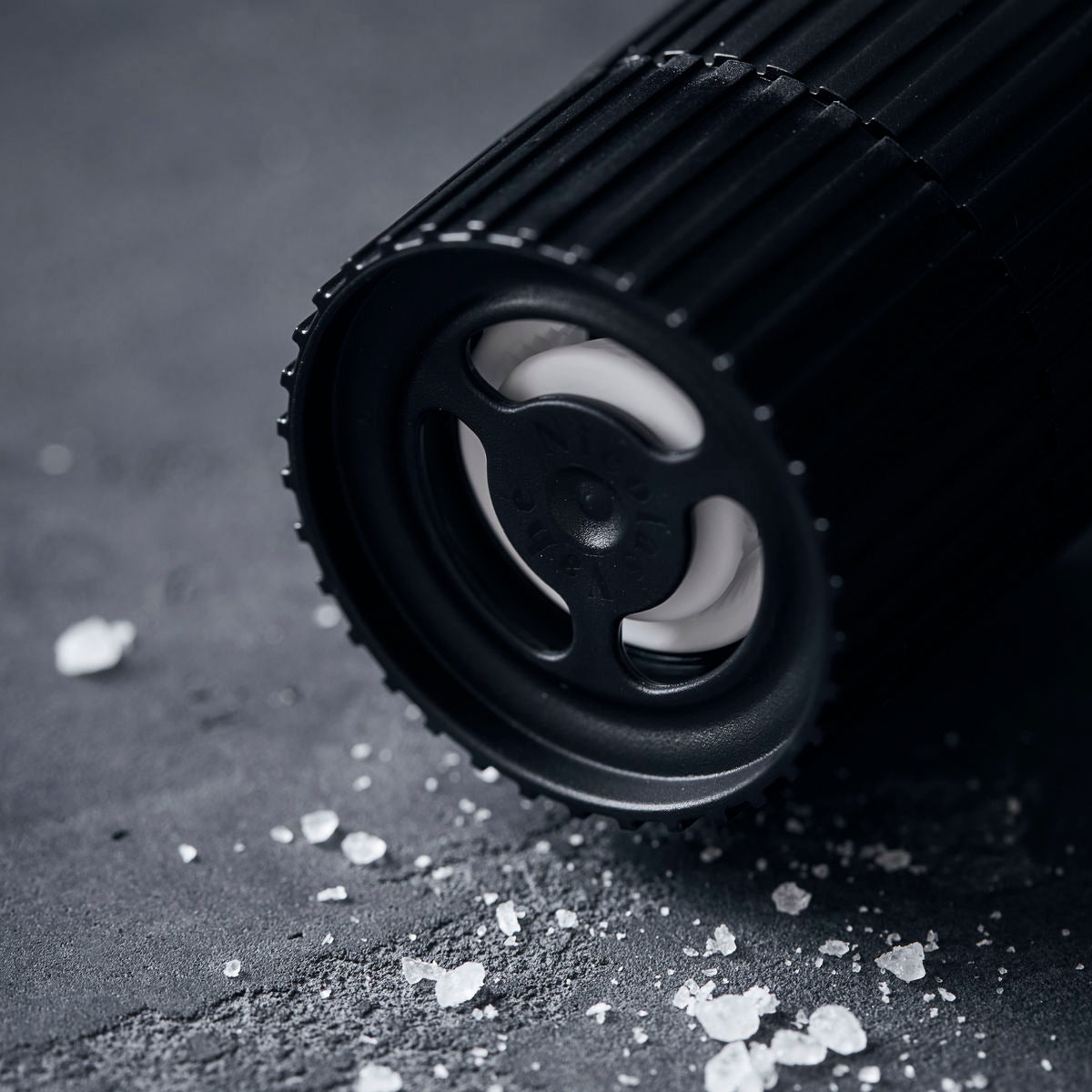 Close-up of a ceramic grinder from Nicolas Vahé lying on a dark surface, surrounded by coarse crystals of French Sea Salt.