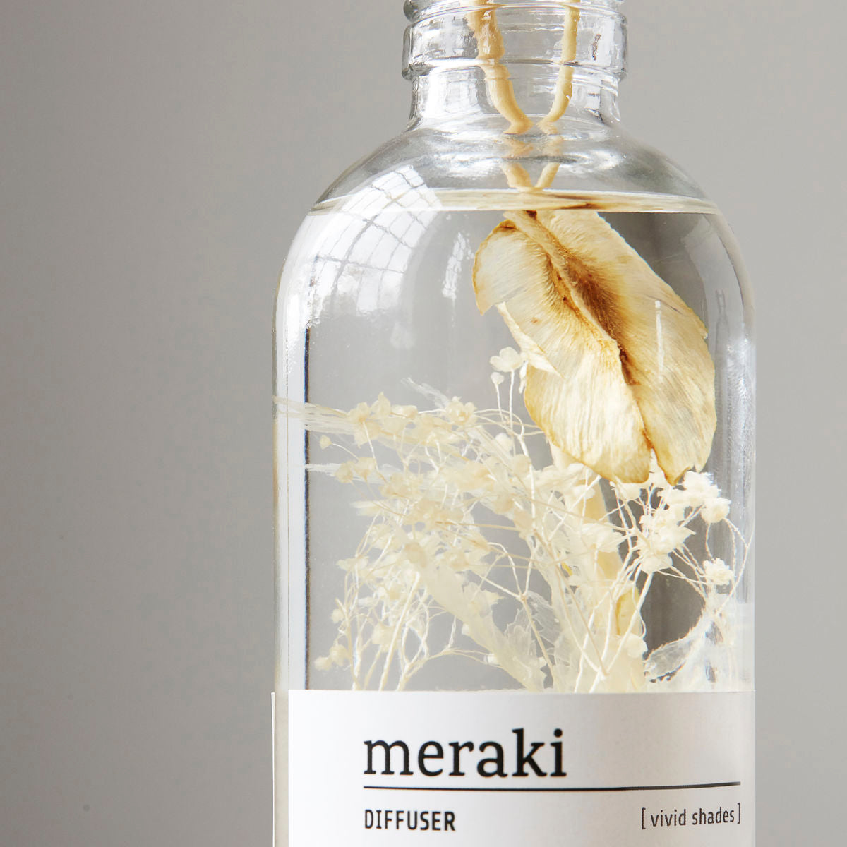 The Meraki Diffuser, Vivid Shades features preserved dried flowers and fragrant liquid in a clear glass bottle—ideal for a calming atmosphere, displayed against a plain gray background.