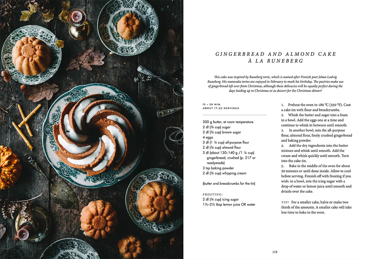 A bundt-style gingerbread and almond cake with white icing sits on a dark table, surrounded by plates and autumnal decor, inspired by classic Nordic desserts—featured beside the recipe text in the Nordic Winter - Cook Book by Cozy Publishing.
