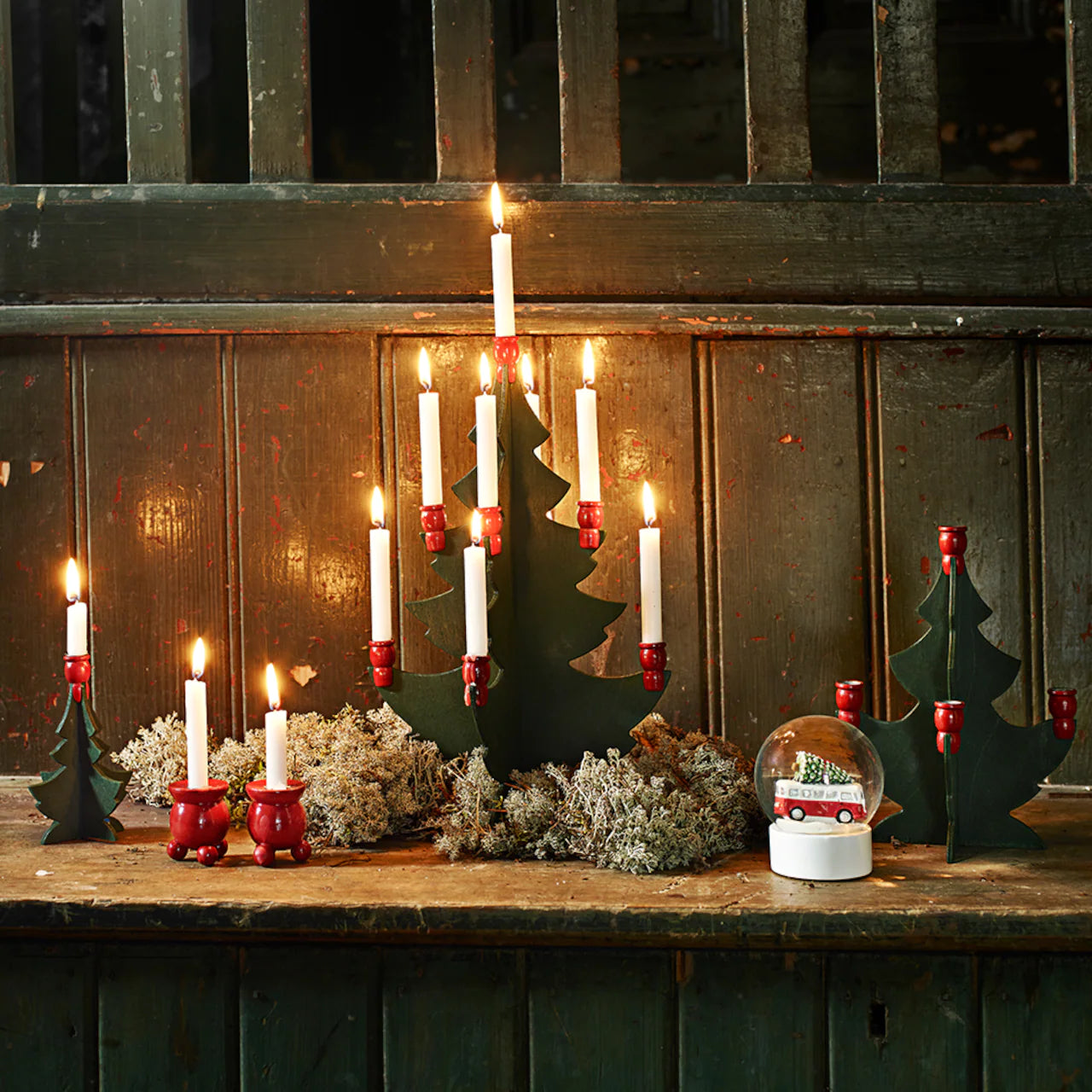 A charming Christmas scene featuring Strömshaga's Christmas Tree w. 1 Candle Holder Small Green/Red in Birch Wood (12.5cm), with a lit candle, moss, and a snow globe for a cozy, traditional holiday touch.