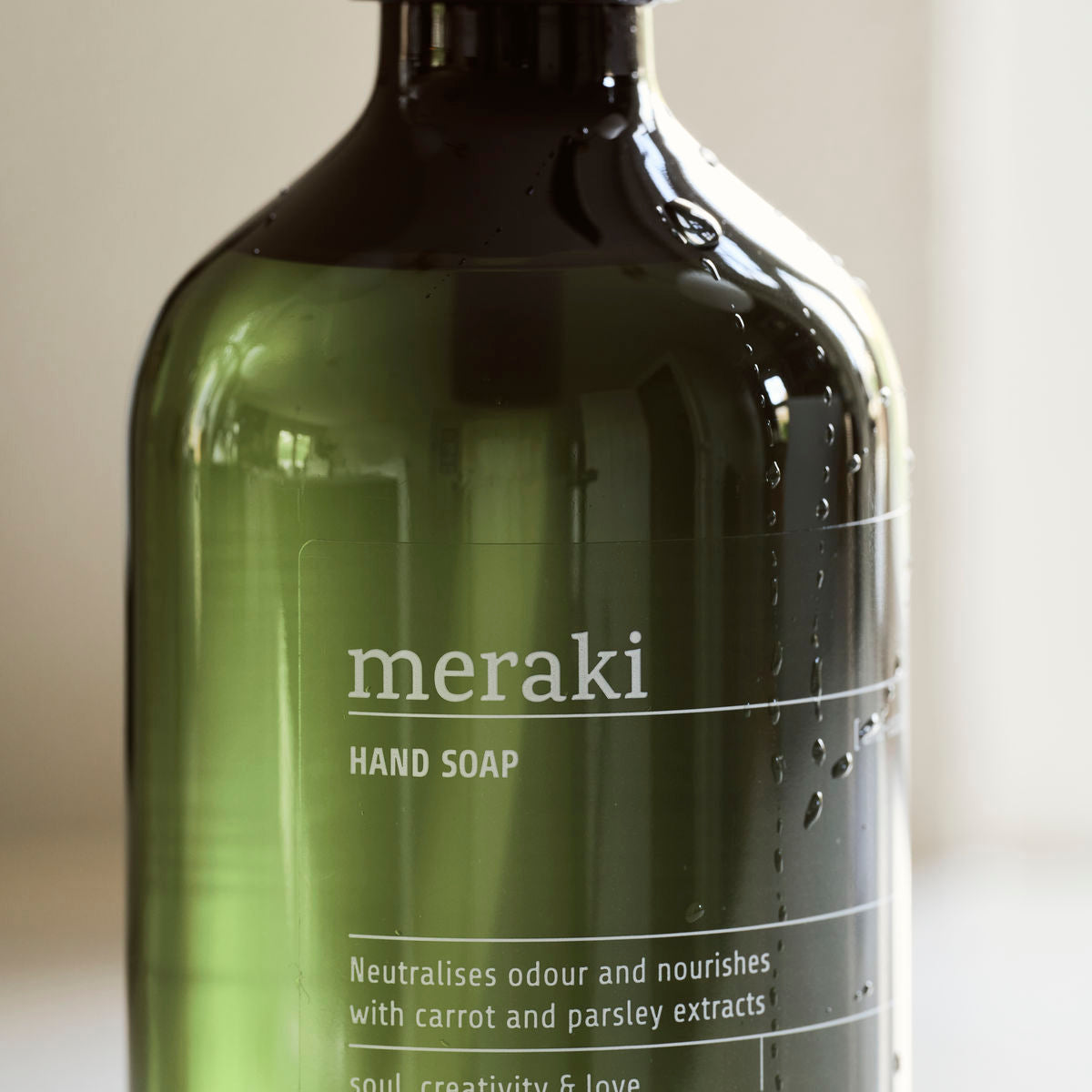 A close-up of a green Meraki Hand Soap, Anti-Odour bottle, showing ingredient details and benefits as an anti-odour hand soap that neutralises food smells, with water droplets visible on its surface.
