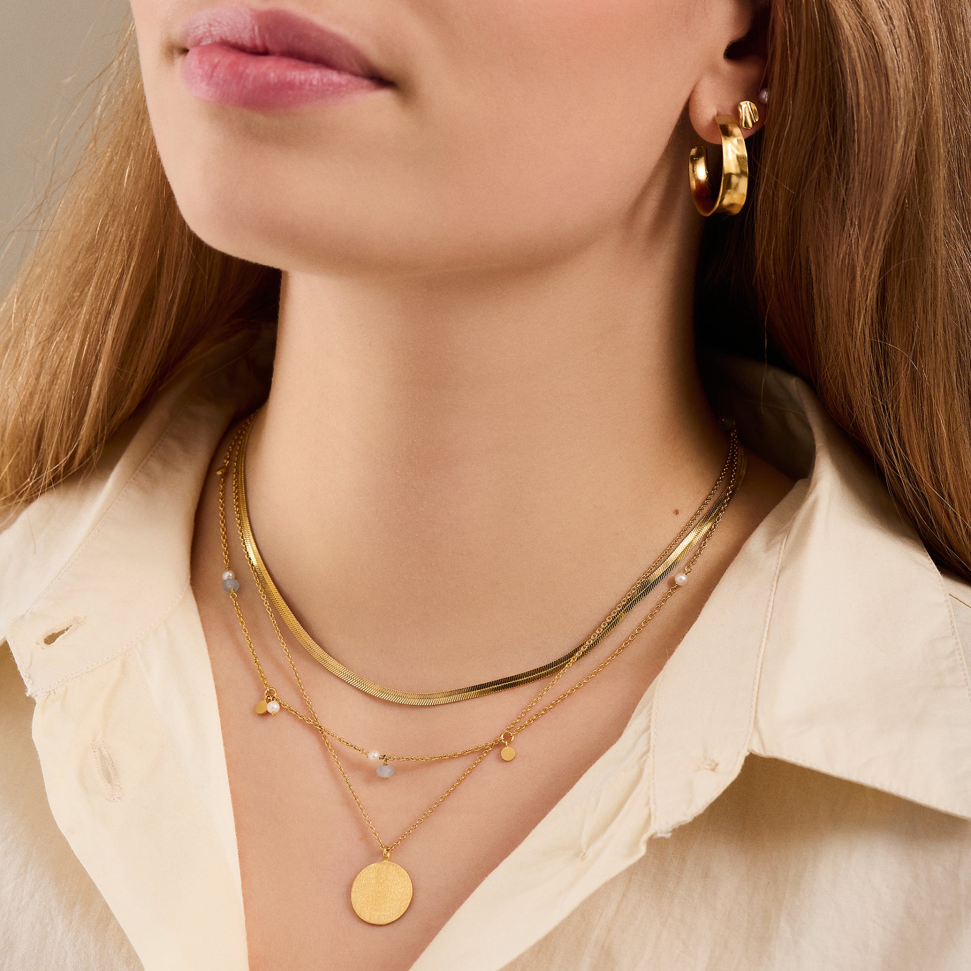 Woman wearing a cream shirt, gold hoop earring, and the Pernille Corydon Afterglow Sea Necklace in Silver with freshwater pearls and blue agate, inspired by natural treasures.