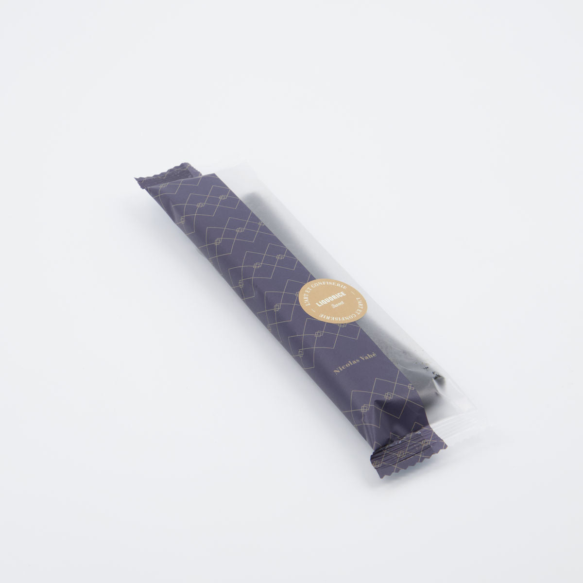 A single wrapped Sweet Soft Liquorice stick from Nicolas Vahé rests in a dark patterned sleeve with a gold sticker on a white background—an elegant and refined gift choice.