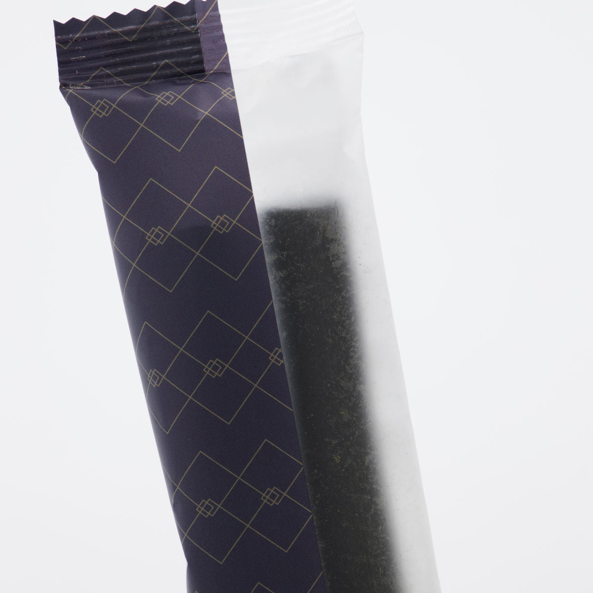 A close-up of a partially opened dark blue wrapper with a geometric pattern reveals a dark, rectangular Sweet Soft Liquorice stick by Nicolas Vahé—an ideal gift for fans of his gourmet treats.