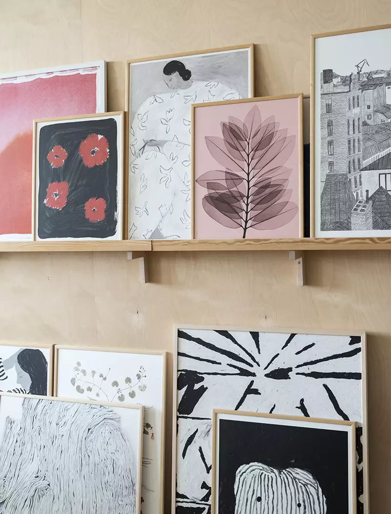 The White Flower Print 50x70 cm by Fine Little Day is displayed among framed abstract and illustrated art prints on two wooden shelves against a light wood-paneled wall.