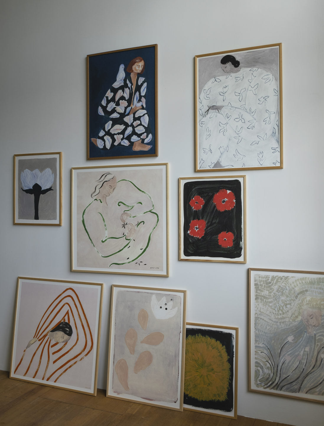 A white wall features the Fine Little Day White Flower Print 50x70 cm, displayed among other framed artworks—some hung and some leaning on a wooden floor.