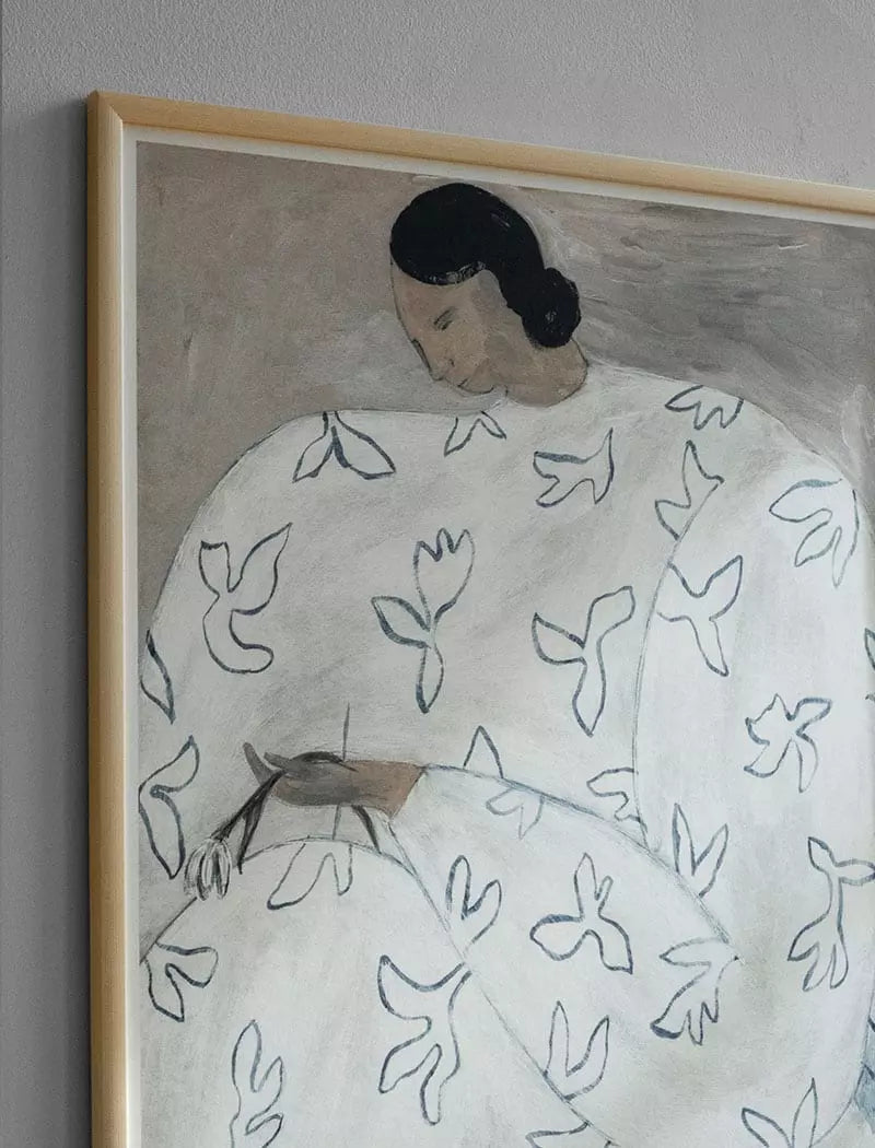 White Flower Print 50x70 cm by Fine Little Day—this framed artwork shows a woman with dark hair in a white robe with blue birds, gazing down while holding a small object against a neutral background.