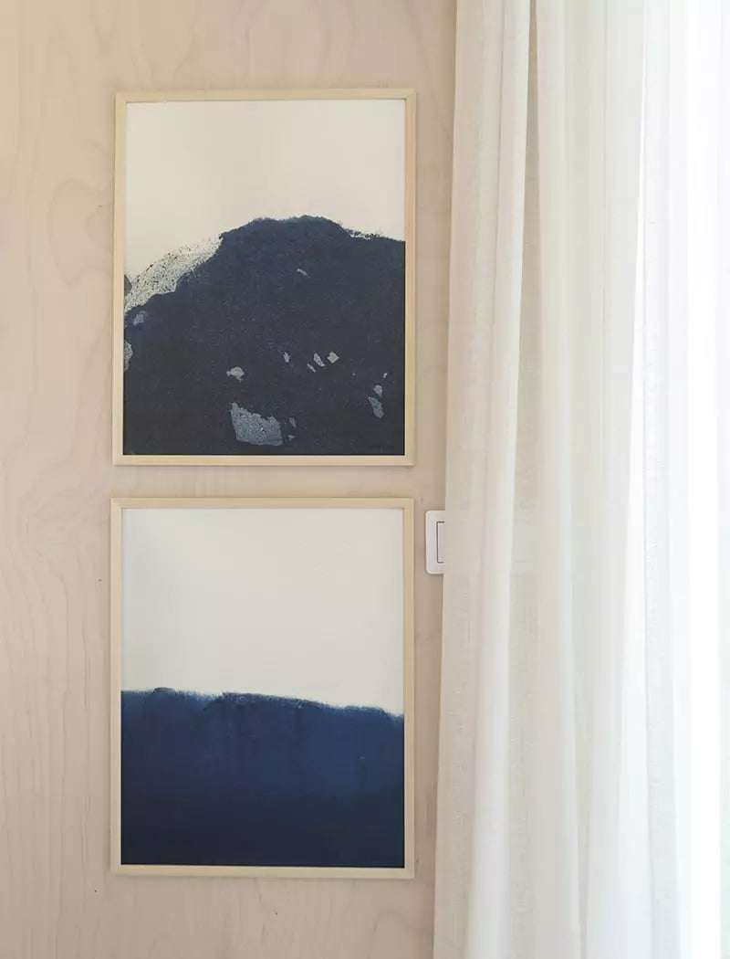 Two Ocean 1 Prints (40x50 cm) by Fine Little Day, featuring deep blue abstract designs, hang vertically on a light wall beside a white curtain.
