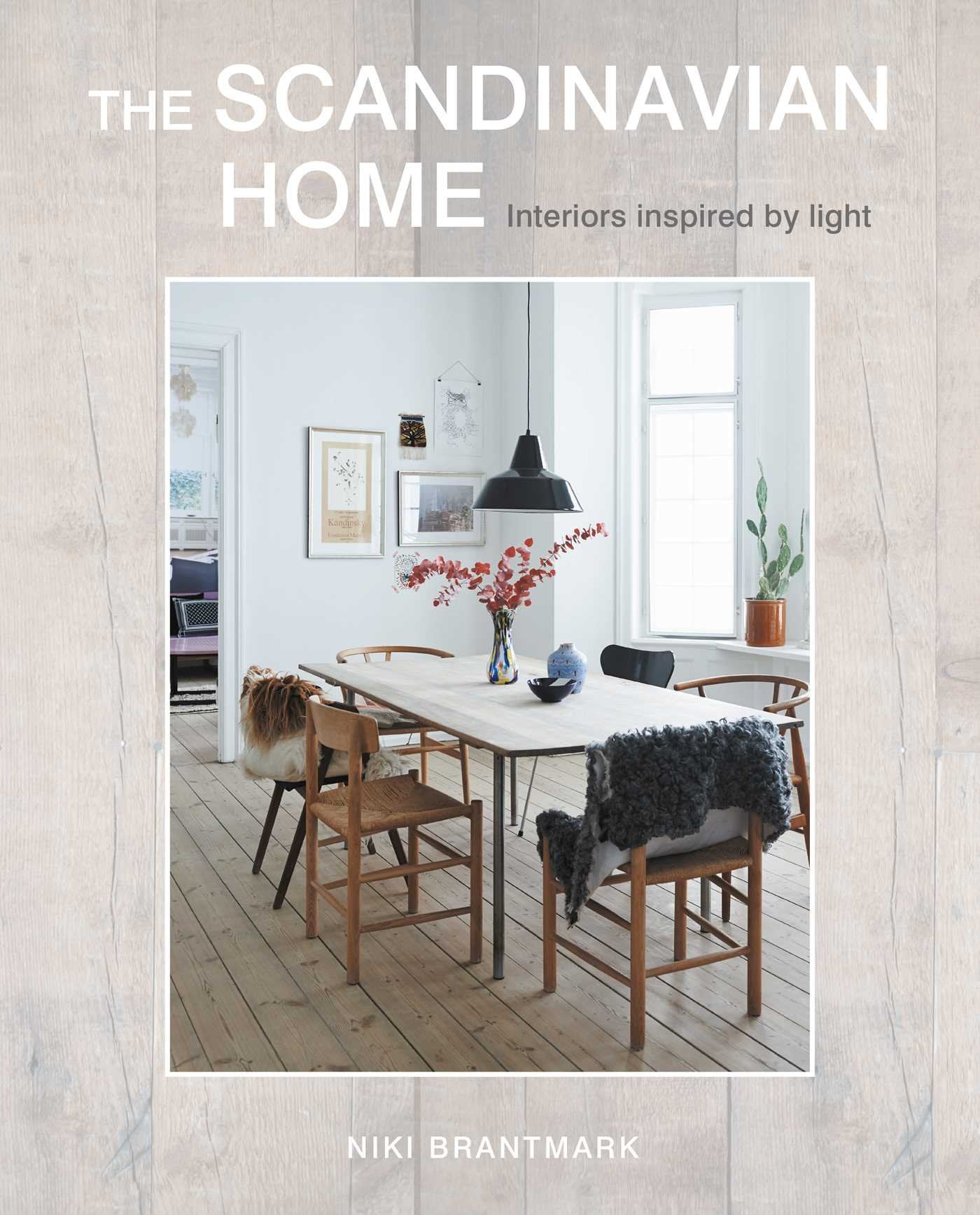 Book cover of The Scandinavian Home - Interiors Inspired by Light by Niki Brantmark, showing a bright dining area with wooden chairs, a white table, and minimalist decor—an ideal example of classic Scandinavian style.