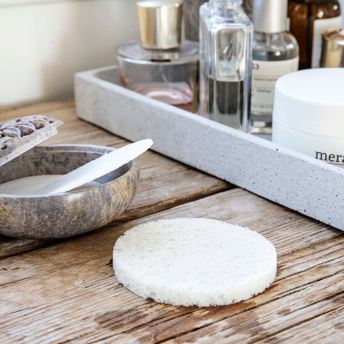 The Meraki Facial Cleansing Sponge, Clean, Reusable lies on a wooden surface next to an open container with a spatula and a tray of skincare bottles—an ideal addition to your daily facecare routine.