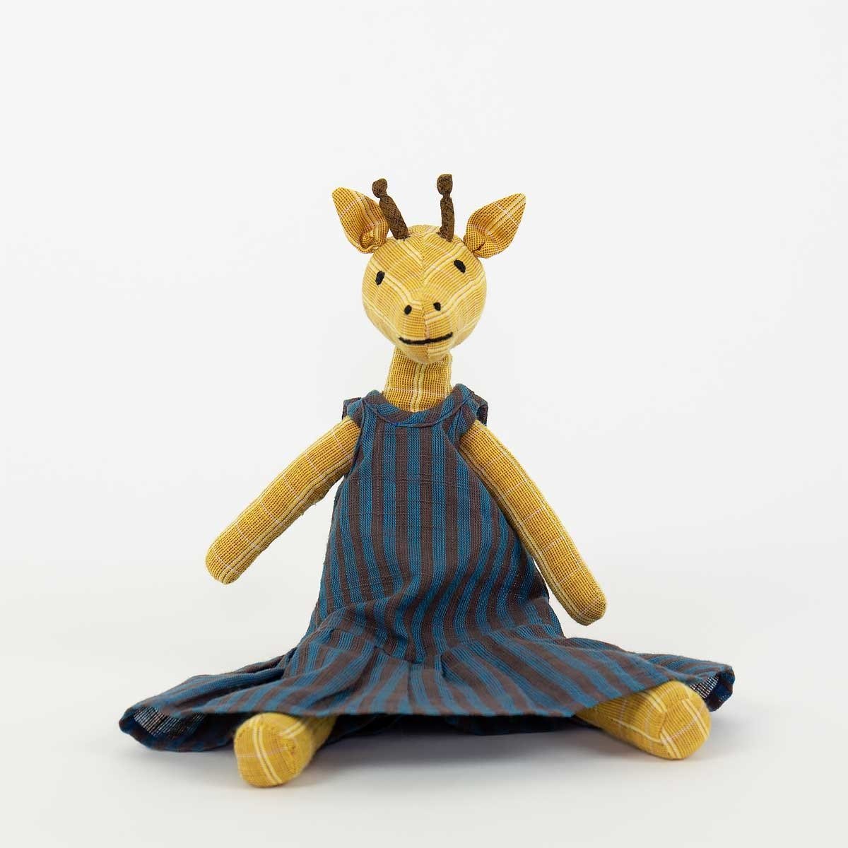 The Giraffe Gaga Soft Toy by A World of Craft, a yellow plush giraffe in a blue and brown striped handwoven cotton dress, sits against a plain white background.