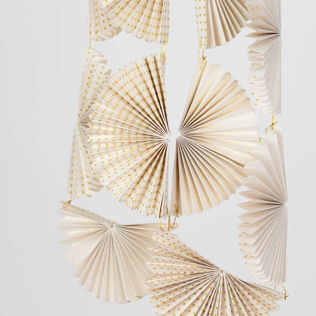 Greta Fold Garland in Gold & White, a handmade paper garland from Bangladesh featuring repeating white fan ornaments decorated with small gold dots.