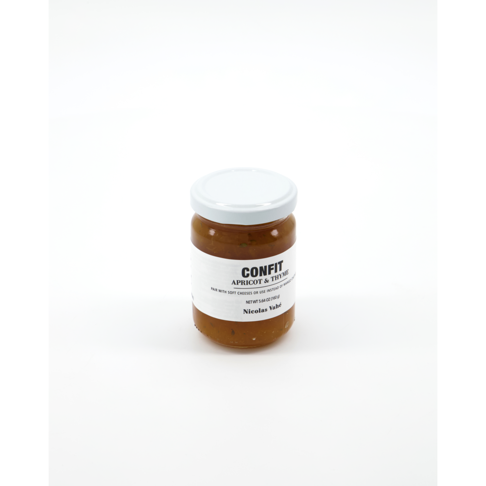 A glass jar of Nicolas Vahé Confit, Apricot & Thyme sits against a white background. The orange preserve, in a simple jar with a white label and black text, is perfect for cheese platters.