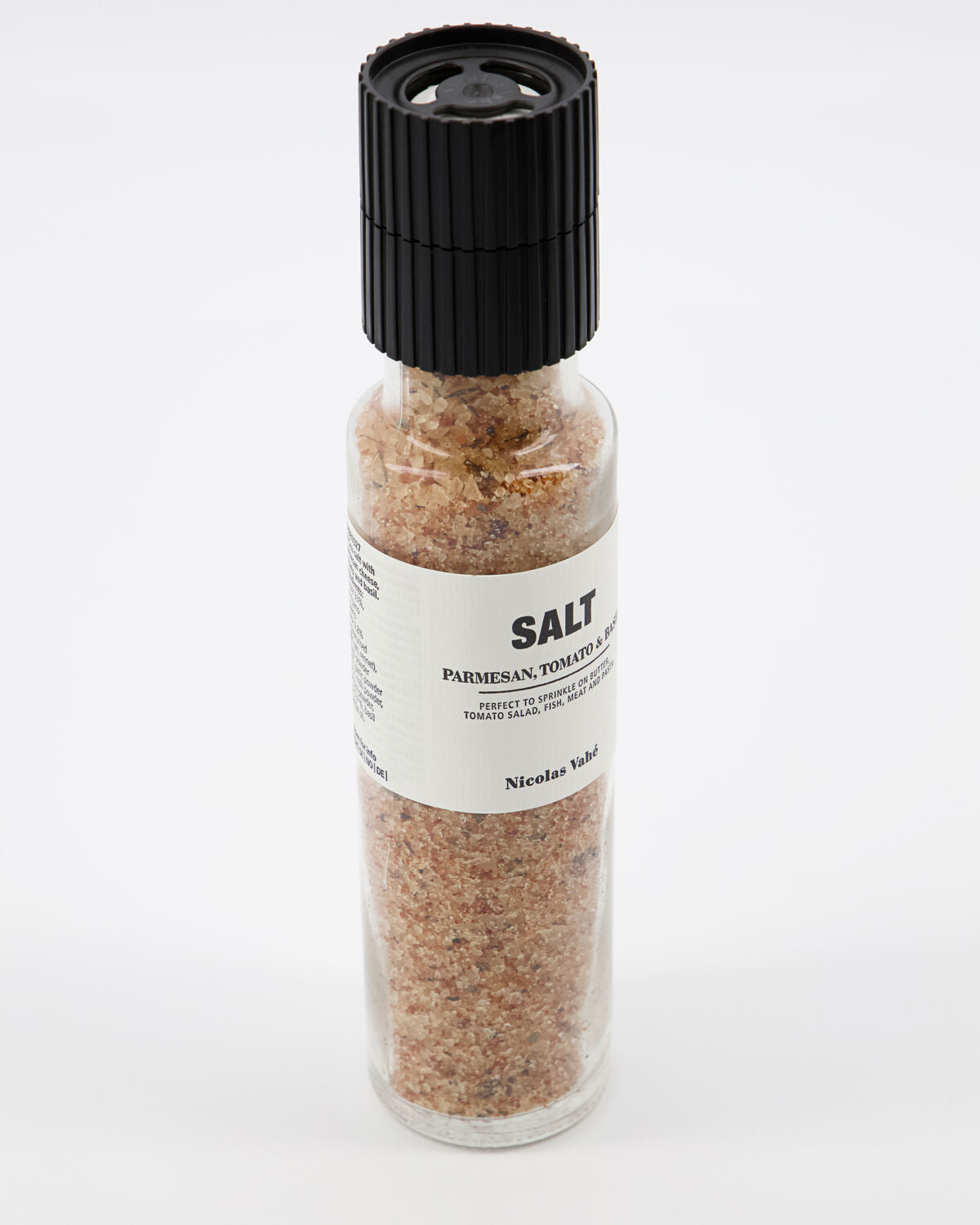 A clear glass salt grinder from Nicolas Vahé, filled with their Salt, Parmesan, Tomato & Basil blend, sits against a white background and showcases a gourmet Mediterranean sea salt infused with parmesan, tomato, and basil flavors.