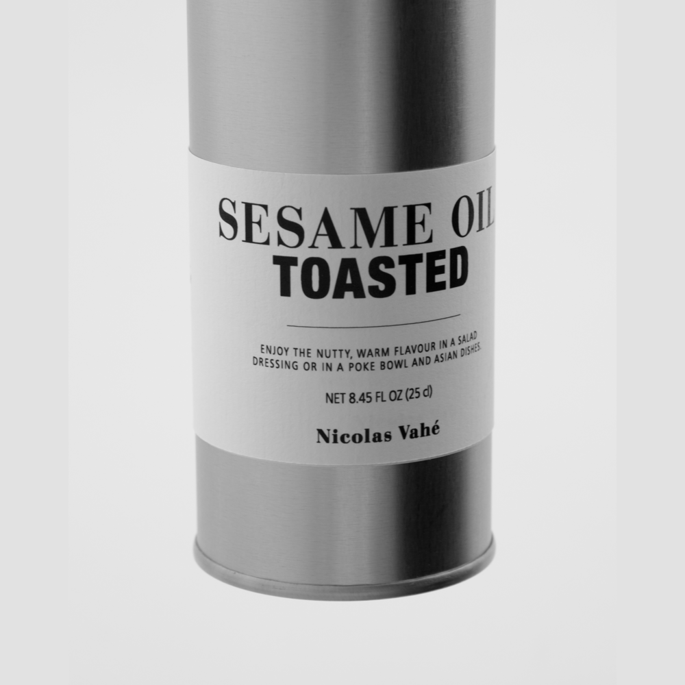 A metal canister labeled Sesame Oil, Toasted by Nicolas Vahé features text about its nutty, warm flavor, recommended as a versatile oil for salads, poke bowls, and Asian dishes. Brand name appears at the bottom.