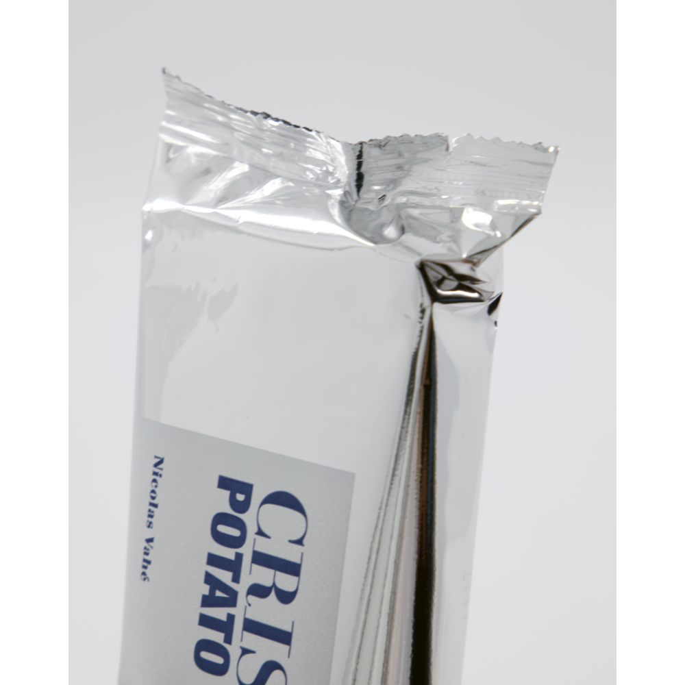 A shiny silver package labeled "Crispy Snack, Potato & Bacon" from Nicolas Vahé, partly opened to reveal the word POTATO and part of CRIS, suggests crispy crisps against a plain light background.