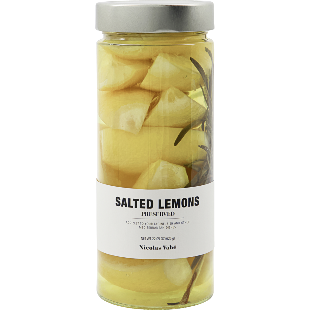A clear glass jar with a silver lid contains yellow salted lemons and herbs in liquid. The label reads “Salted Lemons, Preserved” by Nicolas Vahé—ideal for bringing a zesty touch to Mediterranean recipes.