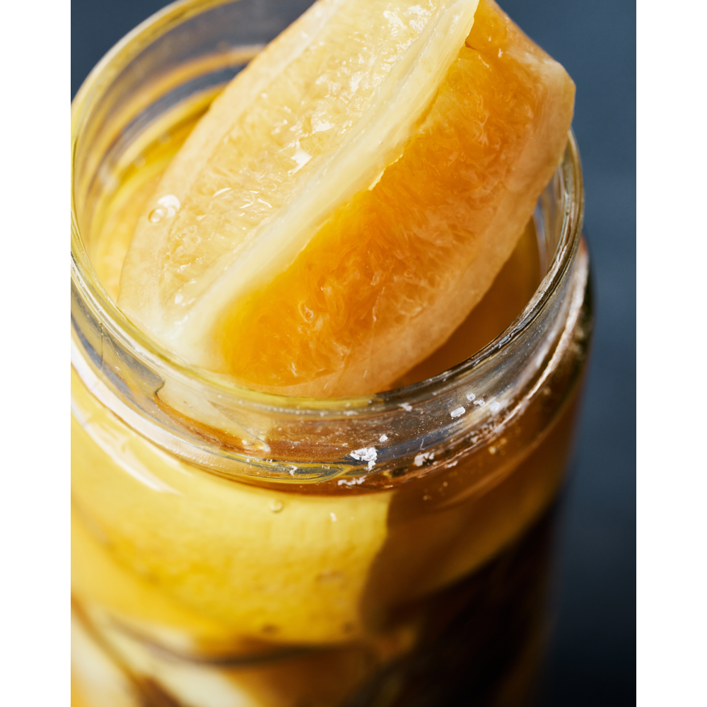 Close-up of Nicolas Vahé Salted Lemons, Preserved, submerged in liquid inside a glass jar. These fresh and juicy lemons are ideal for Mediterranean cuisine or as classic preserved lemons.