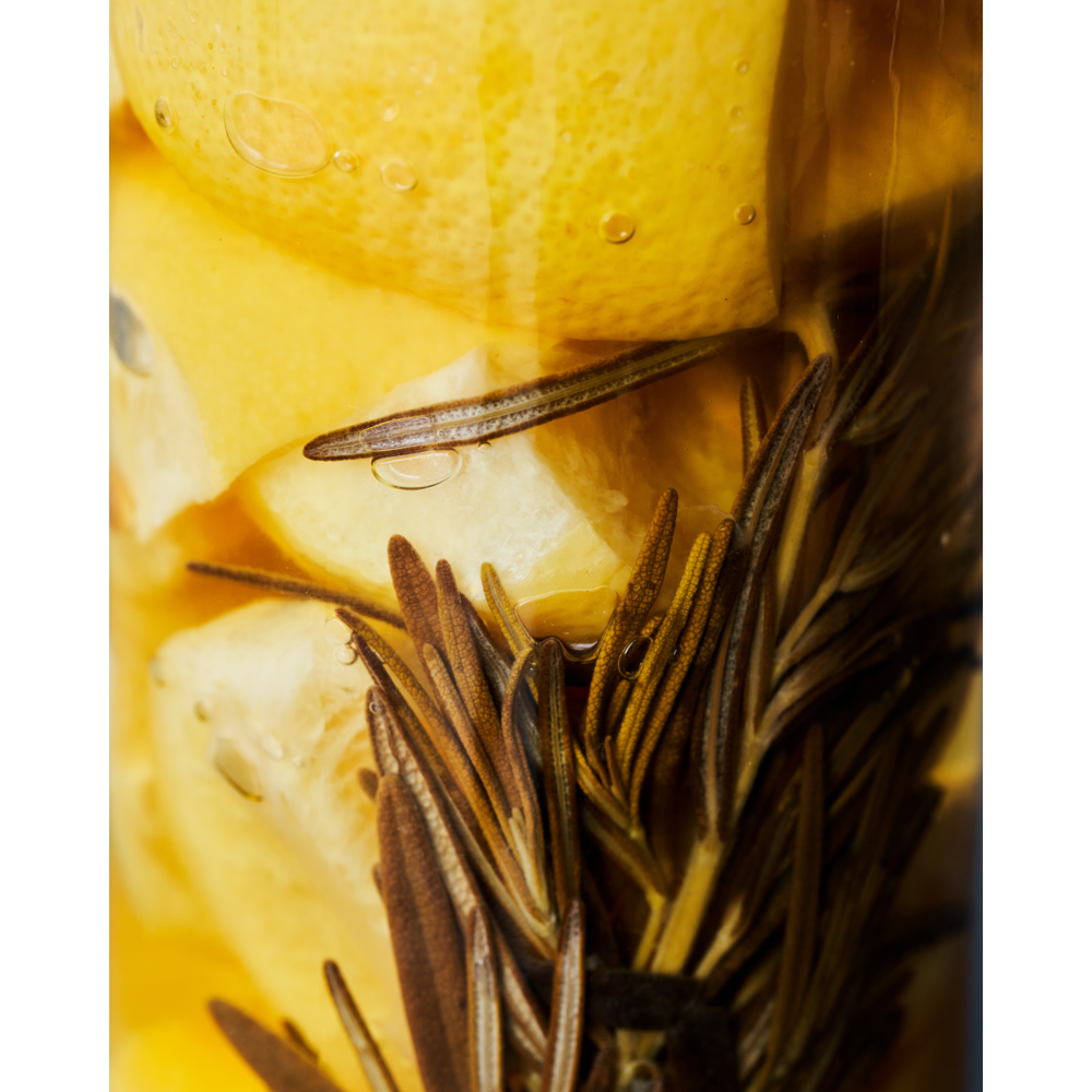 Close-up of lemon slices and rosemary sprigs in bubbly liquid, evoking the tangy flavors of Nicolas Vahé Salted Lemons, Preserved—perfect for infusing drinks or adding a Mediterranean twist to dishes.