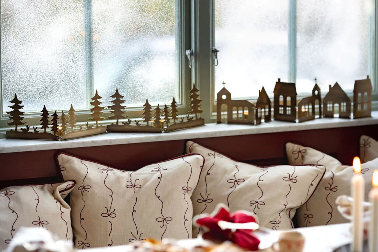 A windowsill features Strömshaga’s Decorative Row City in Antique Brass, while patterned cushions below and a glowing tealight holder on the table create a warm, welcoming ambiance in this cozy space.